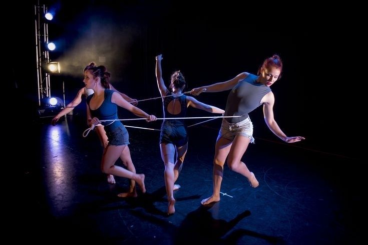 Trois danseuses évoluent dans une lumière scénique en clair-obscur