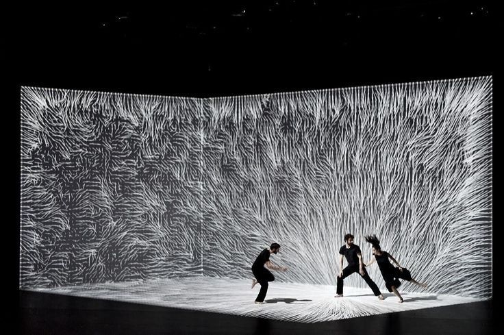 Trois danseurs évoluent devant une projection lumineuse interactive